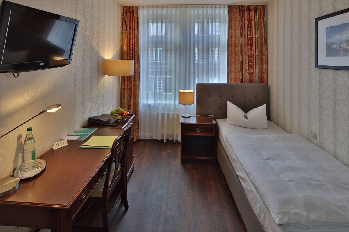 A hotel room with a bed, a desk with a telephone, a television, a lamp, and a window with curtains.