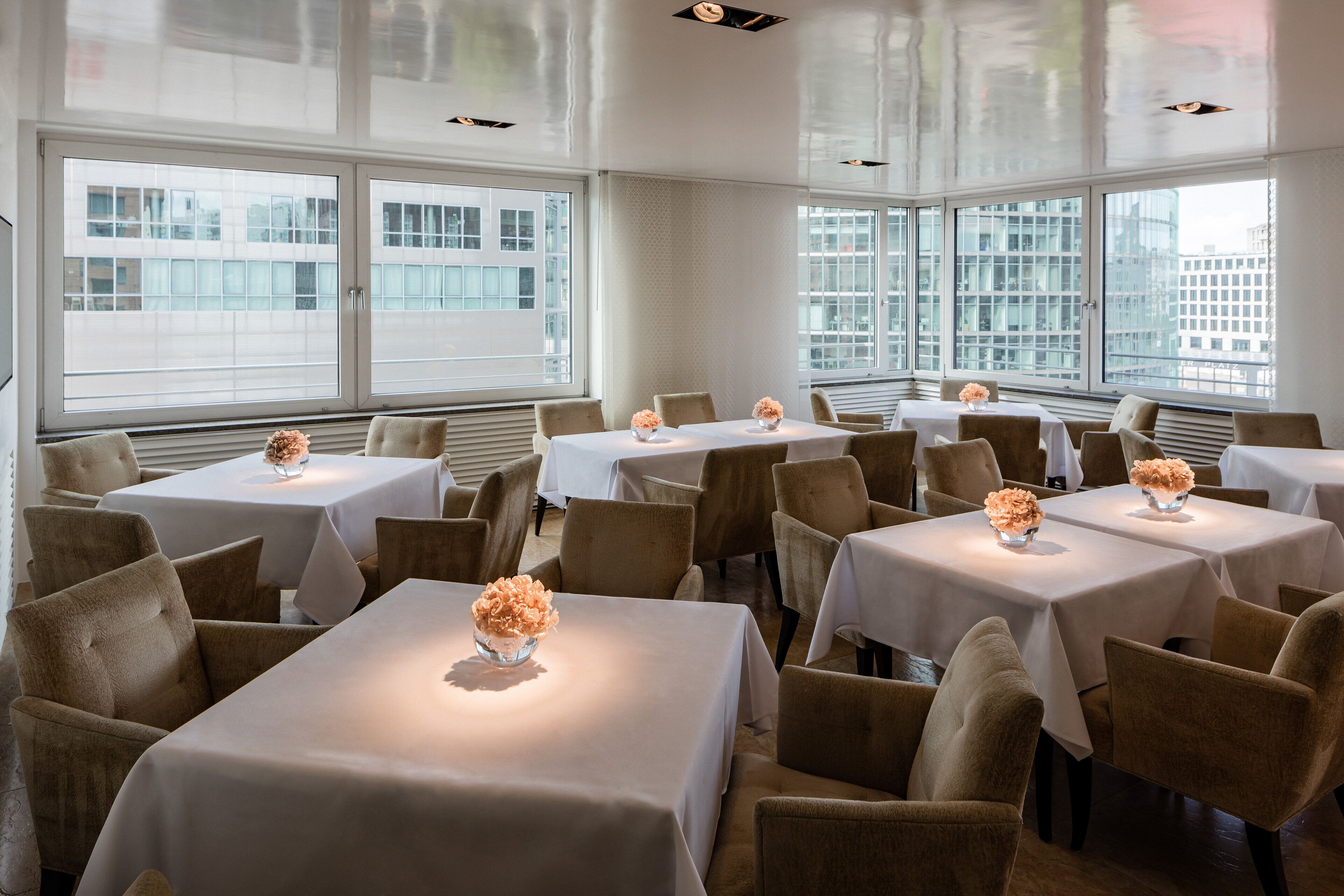 Un comedor con varias mesas y sillas, amplias ventanas con vistas a la ciudad y un diseño interior moderno.