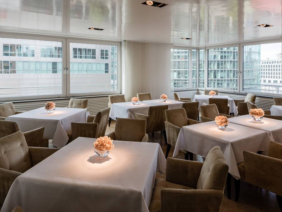 Un comedor con varias mesas y sillas, amplias ventanas con vistas a la ciudad y un diseño interior moderno.