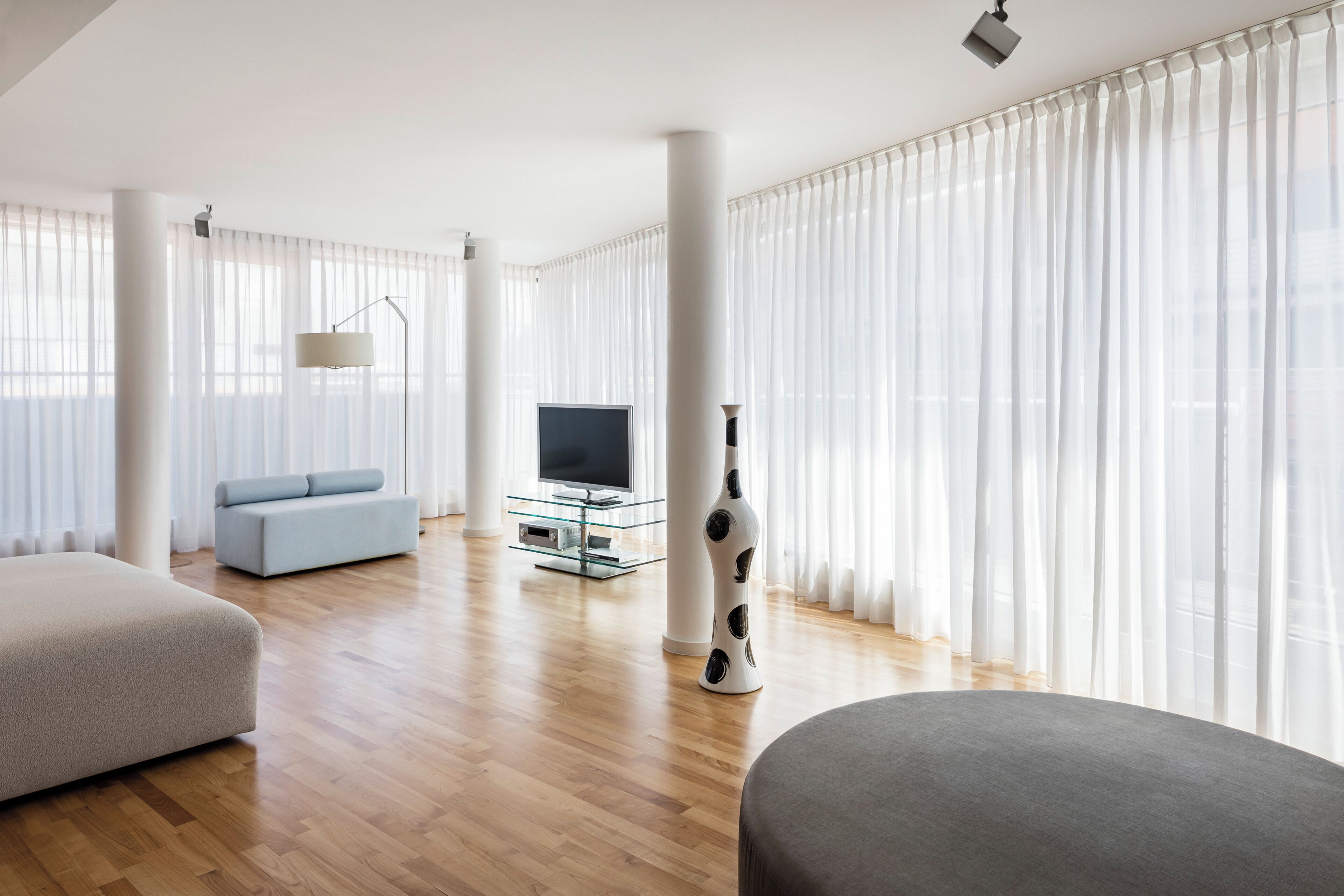 A modern living room with a sofa, a television on a glass stand, and a decorative vase.