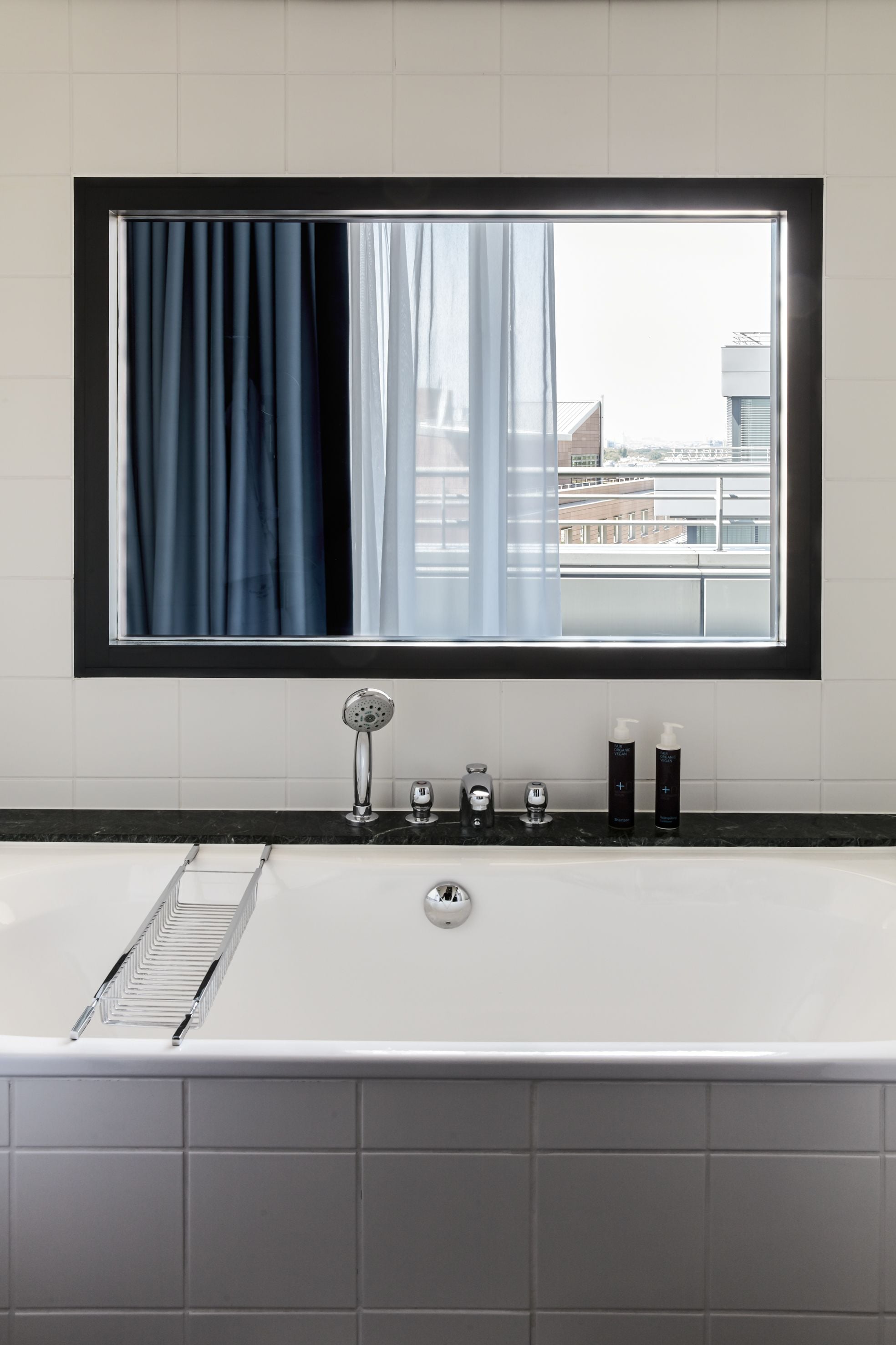 A modern bathroom with a large bathtub, a window with curtains, and a view of buildings outside.