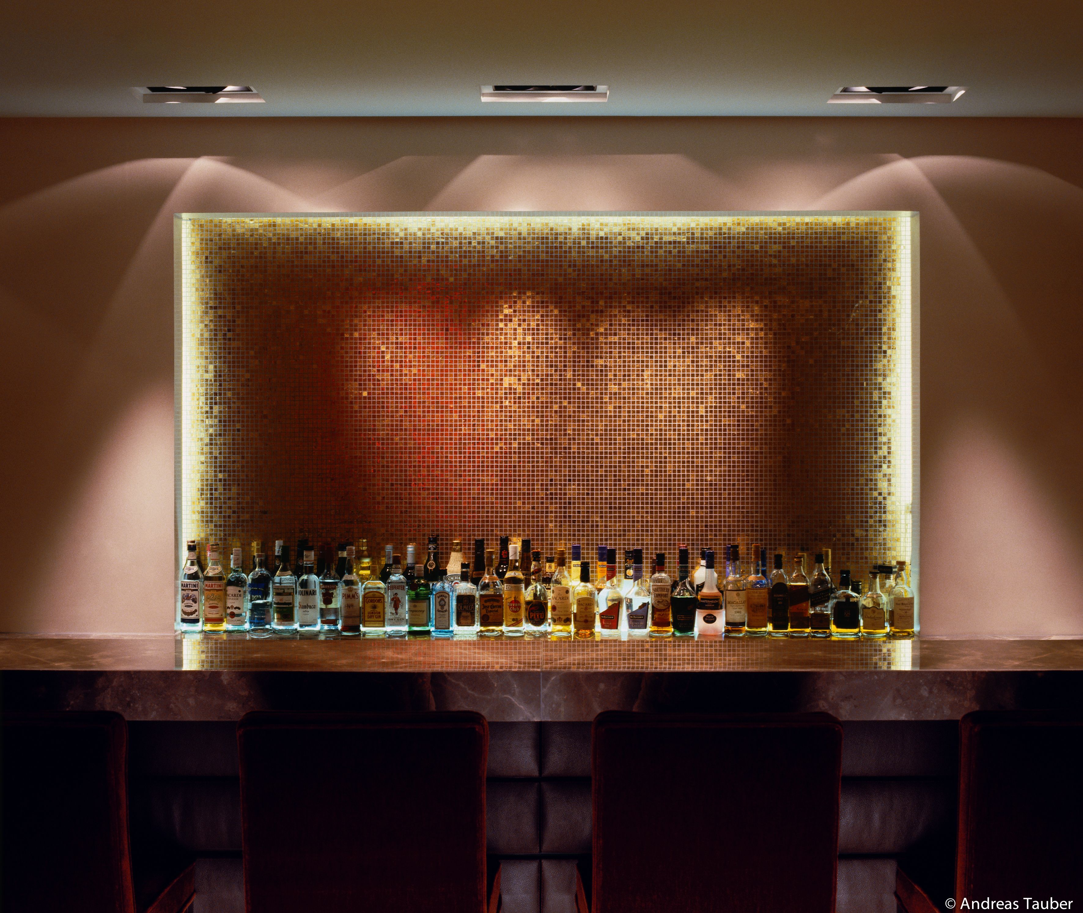 Een bar met een betegelde muur met mozaïek en diverse drankflessen.