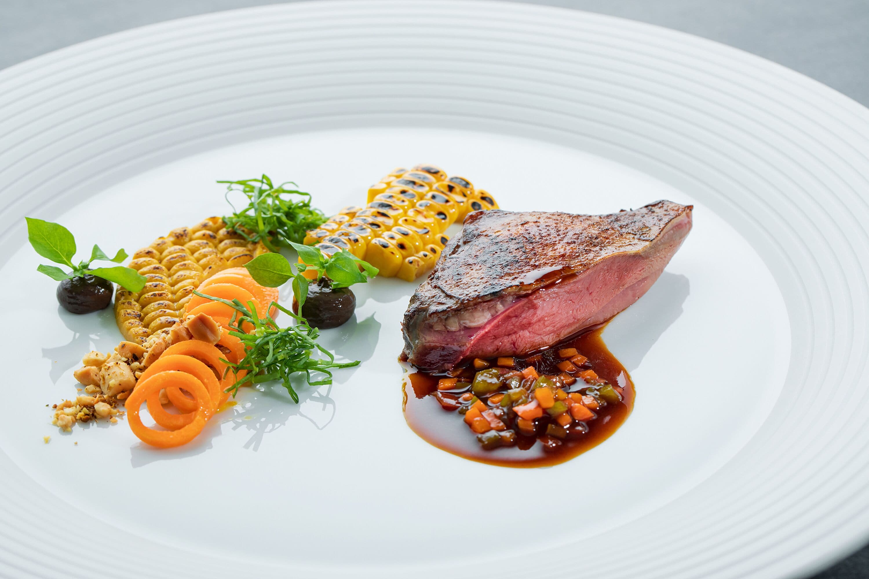 A white plate with a steak, grilled corn, and a vegetable medley.
