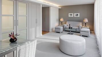 Et moderne hotelværelse med et glas spisebord, en rund skammel, en sofa, to sengeborde med lamper og en stor seng.