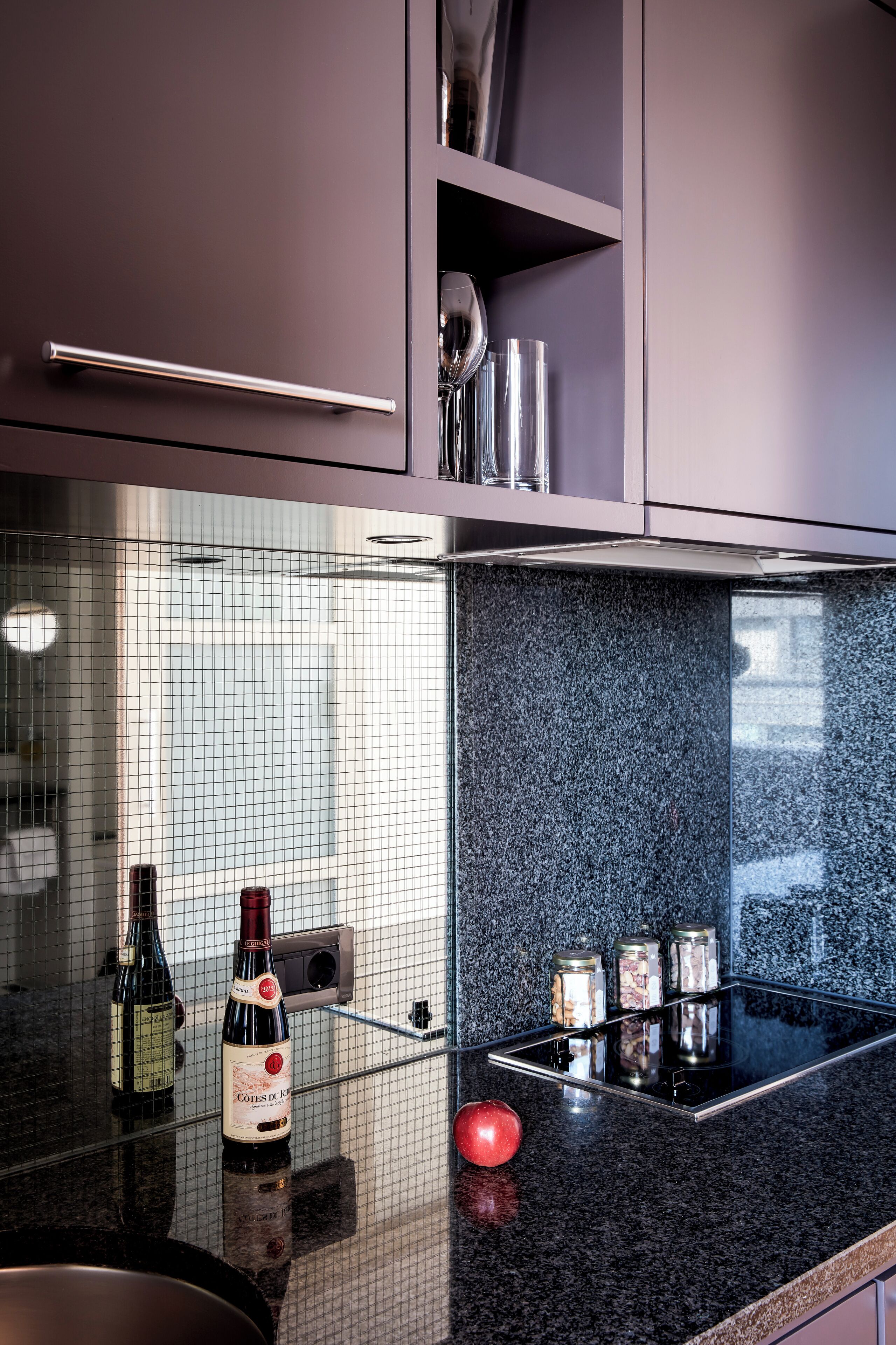 Una cocina con encimera de granito, una botella de vino y una manzana roja.