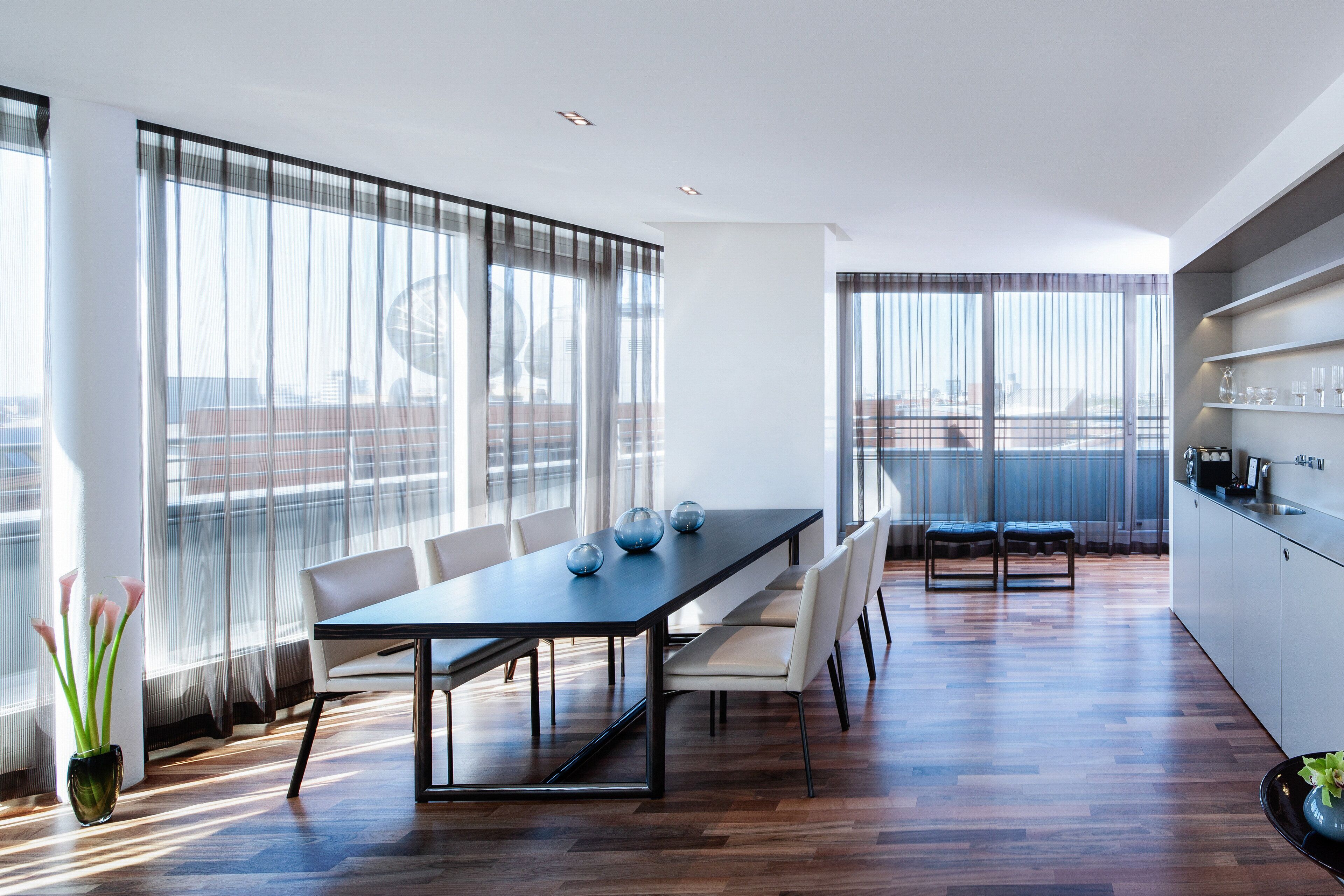 Un comedor moderno con una mesa larga, sillas y vistas de la ciudad a través de grandes ventanales.