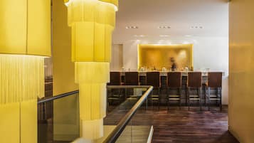 Un área de bar moderna con barandilla de vidrio, suelo de madera y una barra con taburetes.