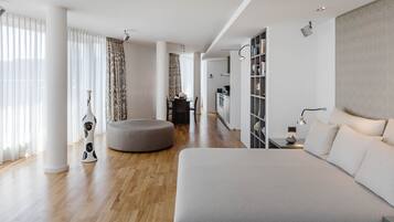 Habitación de hotel moderna con una cama grande, un área de descanso y una cocina al fondo.