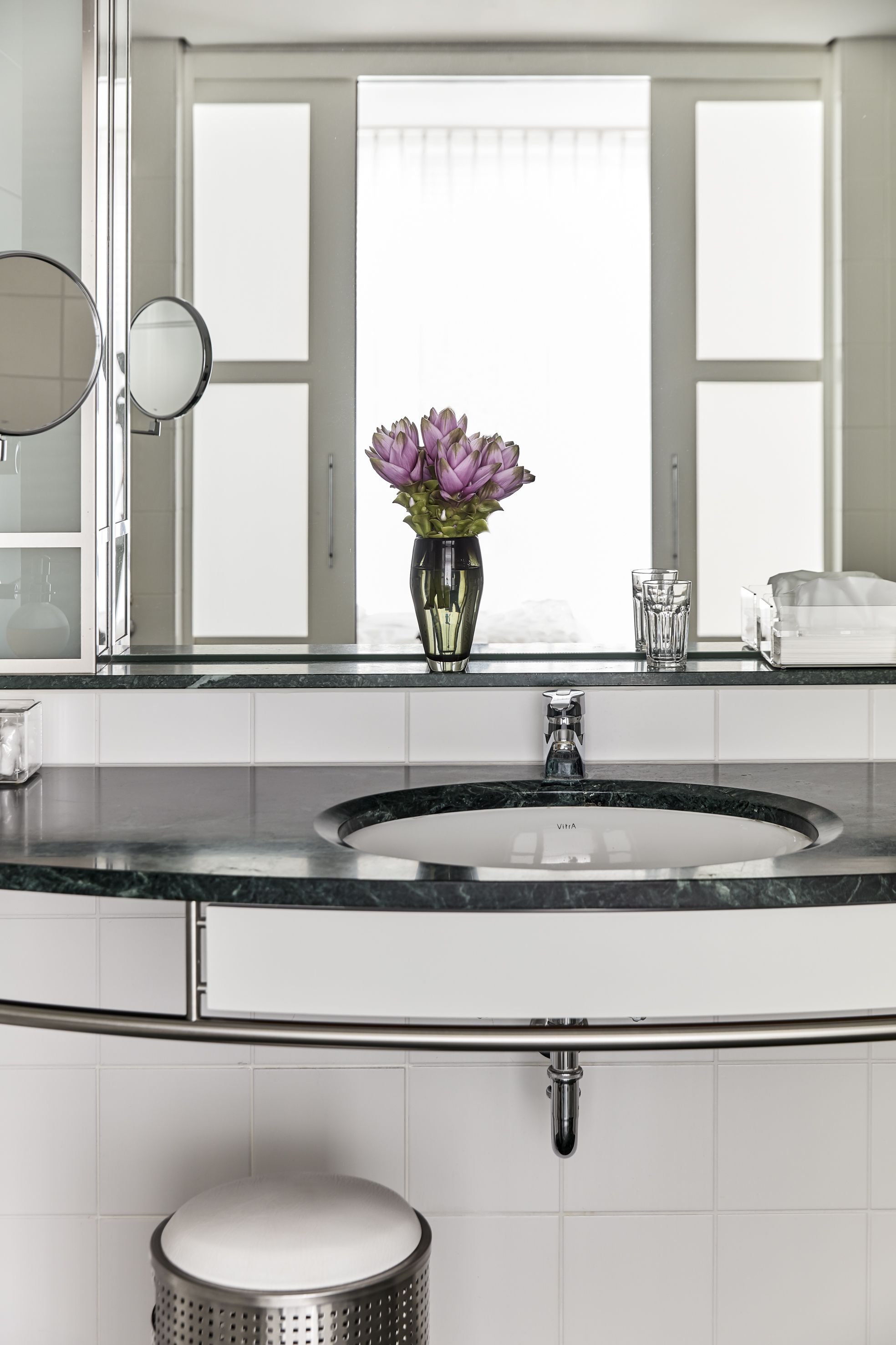 Un baño moderno con un lavabo redondo, un espejo y un florero con flores.
