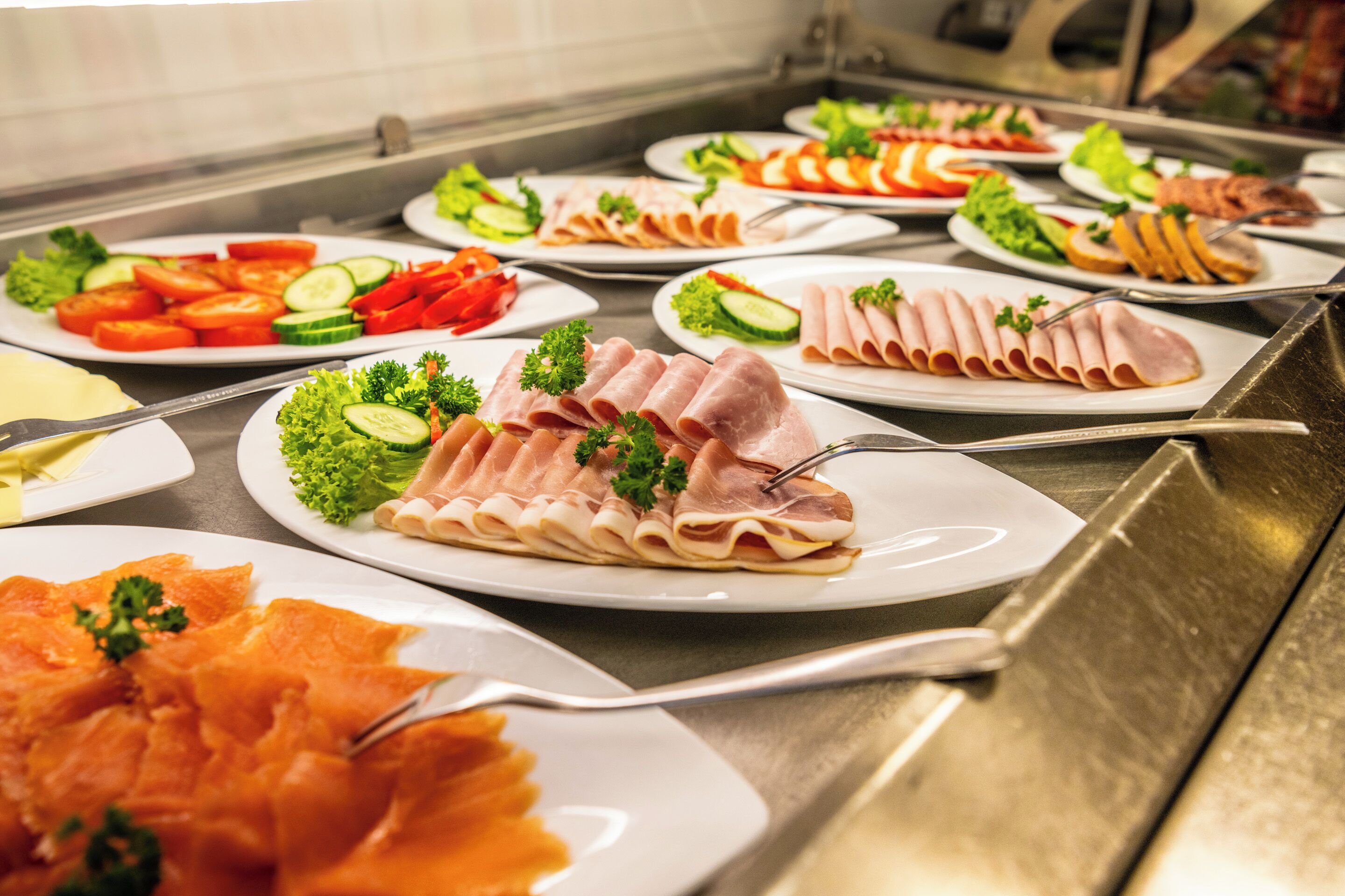 Un bufé con diversas opciones de comida, incluyendo carnes cortadas, verduras y ensaladas.