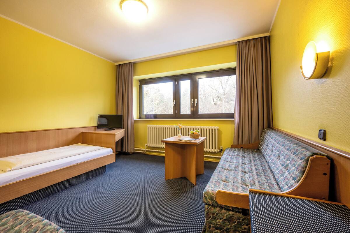 A compact hotel room with a bed, a sofa, a small table, and a television.