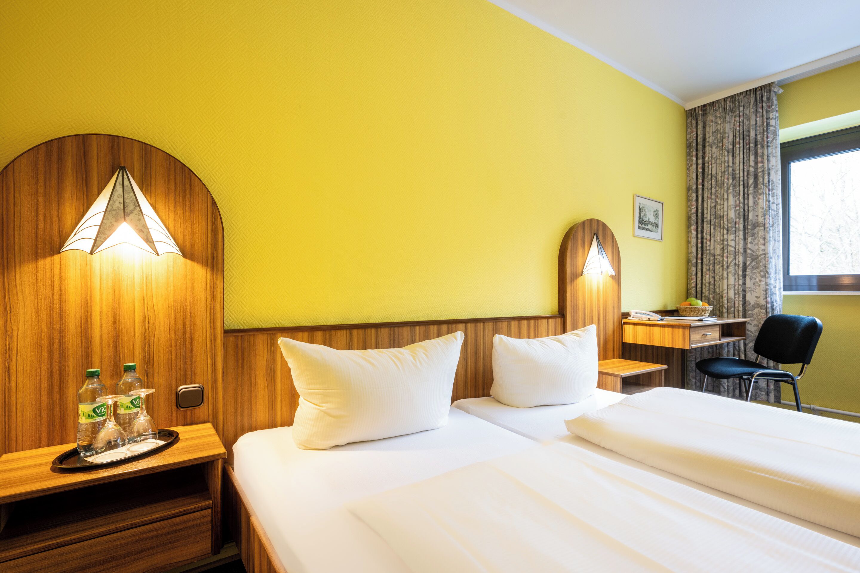 A hotel room with a bed, two bedside tables, a desk, and a chair.