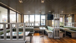 A restaurant interior with high ceilings, grid-patterned ceiling, large windows, and green cushioned seating.