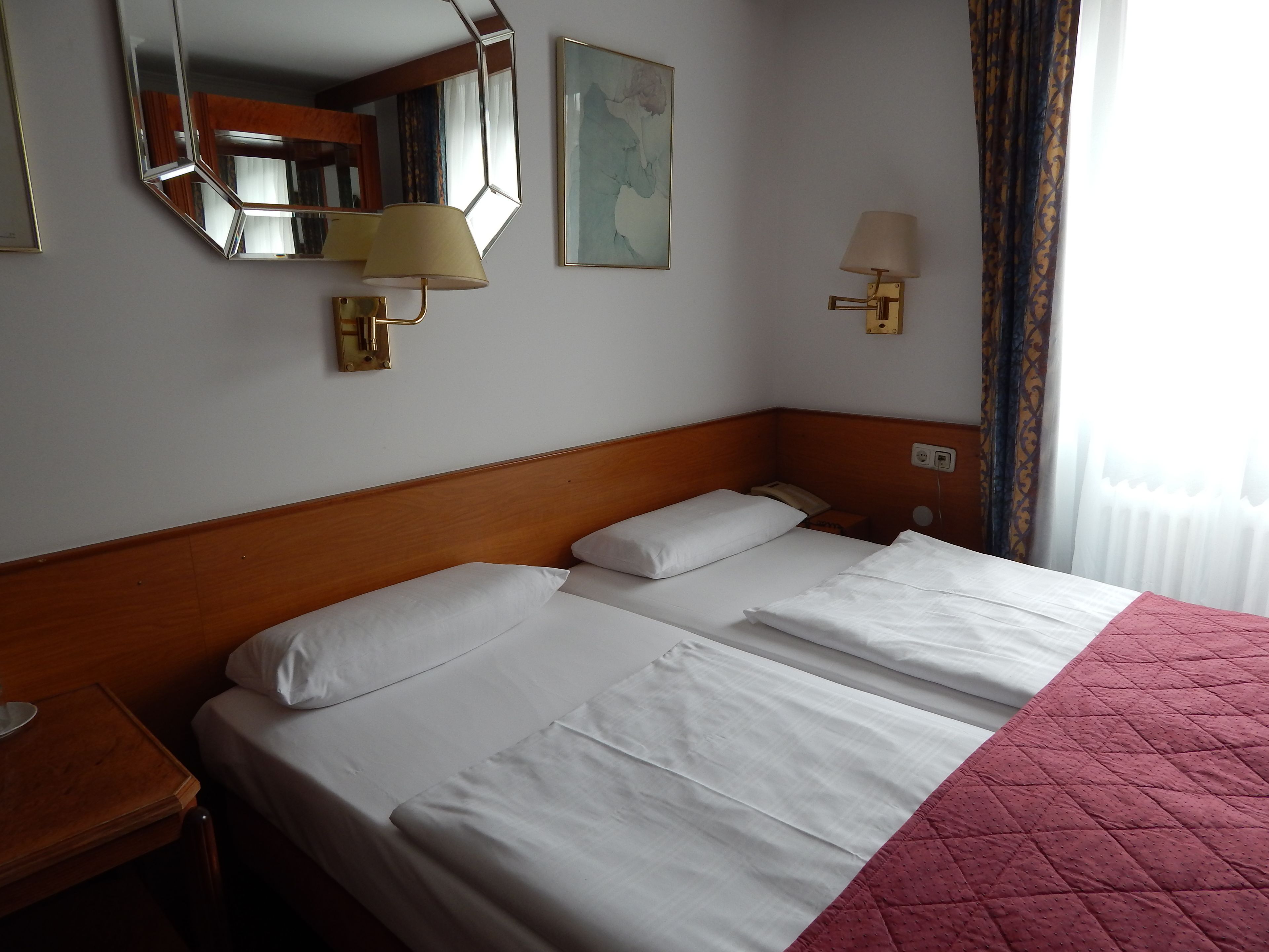 A hotel room with a large bed, a nightstand, a lamp, a mirror, and a painting on the wall.