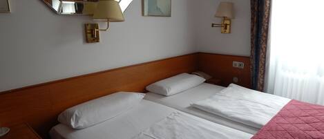 A hotel room with a large bed, a nightstand, a lamp, a mirror, and a painting on the wall.