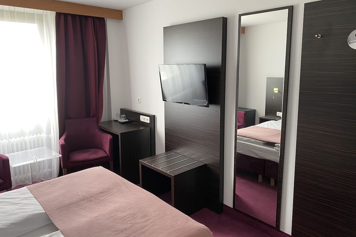 Ein Hotelzimmer mit Bett, Schreibtisch, Stuhl, Fernseher und einem großen Spiegel.