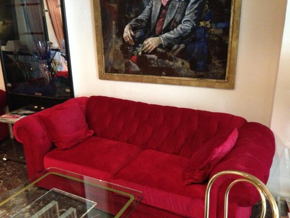 A red sofa in a room with a painting on the wall and a glass coffee table in front. - Montree Hotel (Munich)