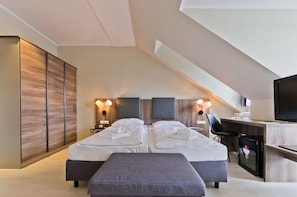 A modern hotel room with two beds, a desk, a chair, and a television.