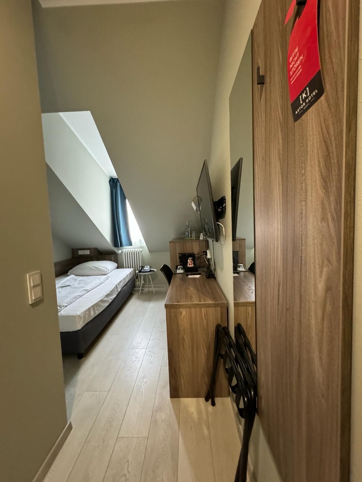 A compact room with a bed, a desk, and a TV. There is a window with a view of the sky.