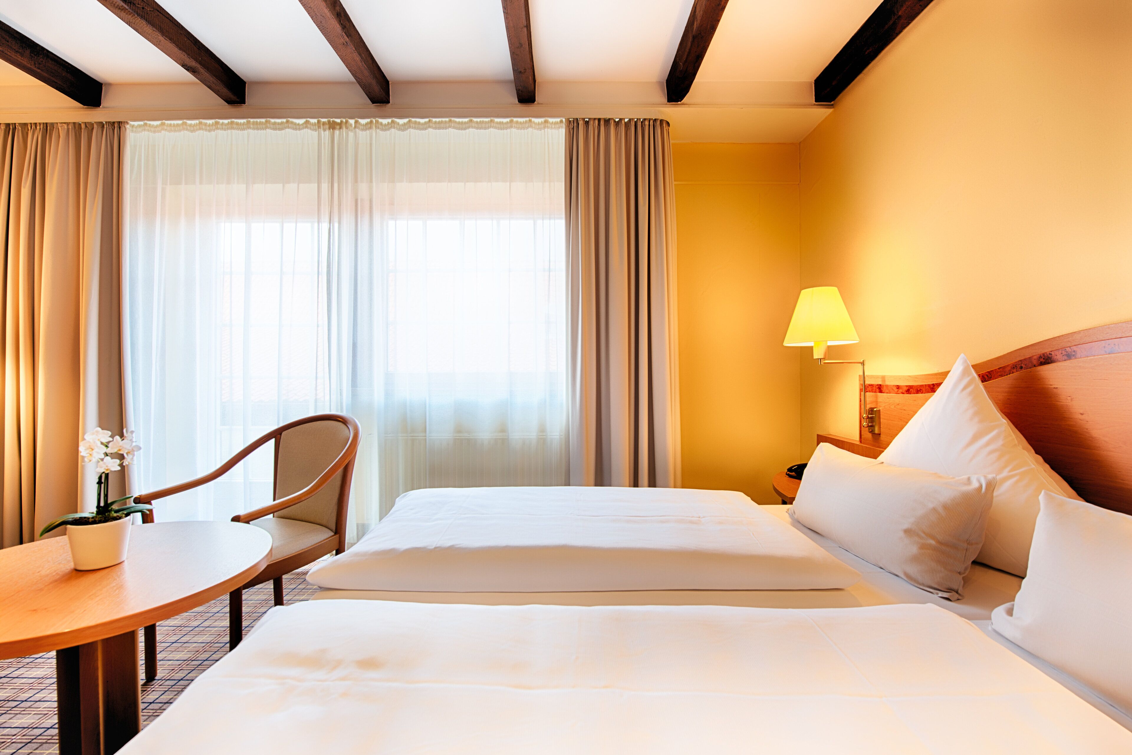 A hotel room with a bed, a chair, a small table, and a lamp.