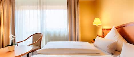 A hotel room with a bed, a chair, a small table, and a lamp.
