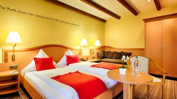 Habitación de hotel con una cama grande, dos mesitas de noche con lámparas, una pequeña mesa con una planta y vasos, y un armario.