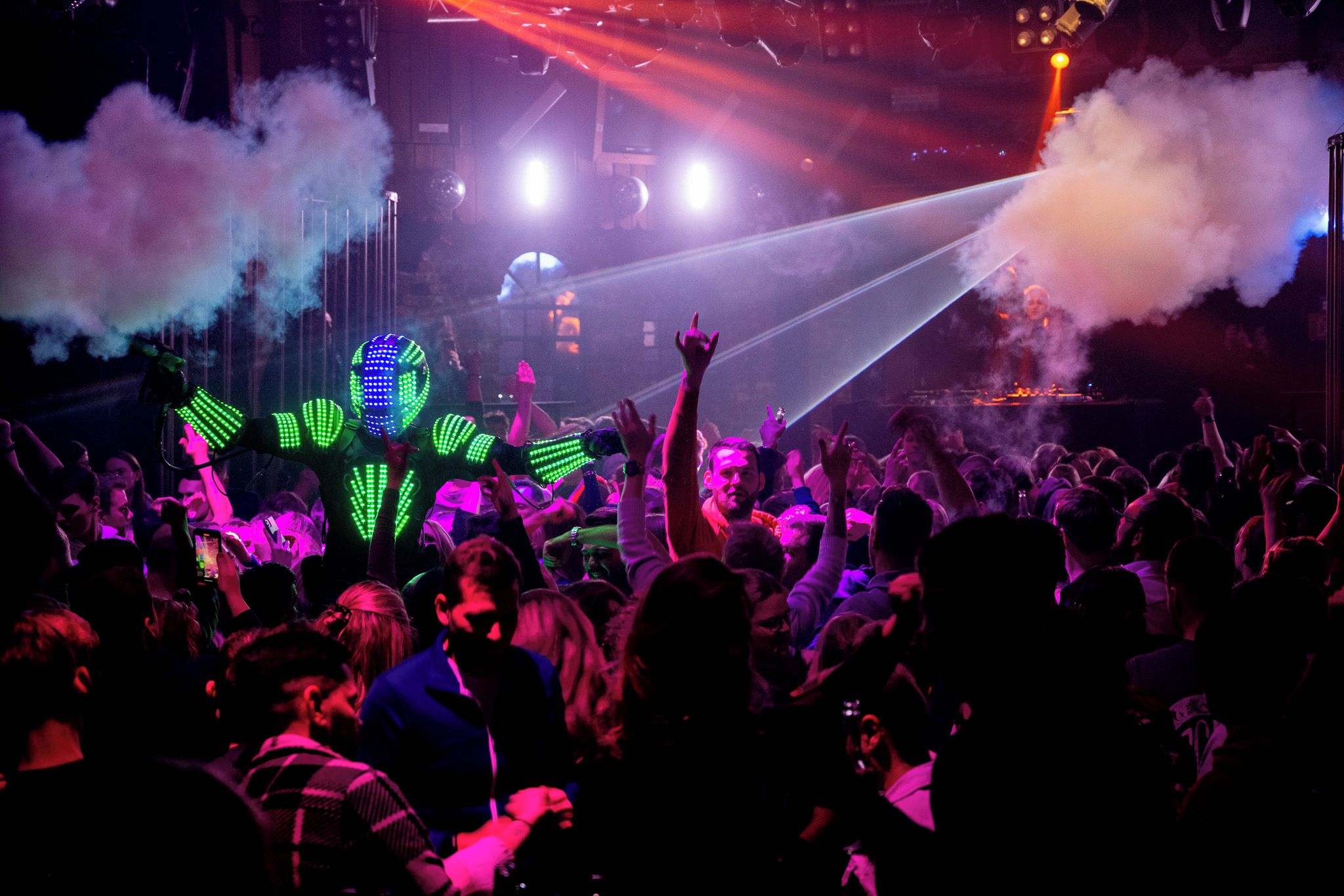 Un evento multitudinario en interiores con luces de escenario y efectos de humo.
