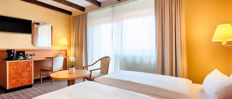 A hotel room with a bed, a desk, a chair, a small table, a lamp, and a TV.
