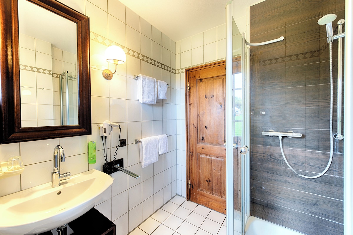 A bathroom with a sink, mirror, towel rack, shower, and wooden door.