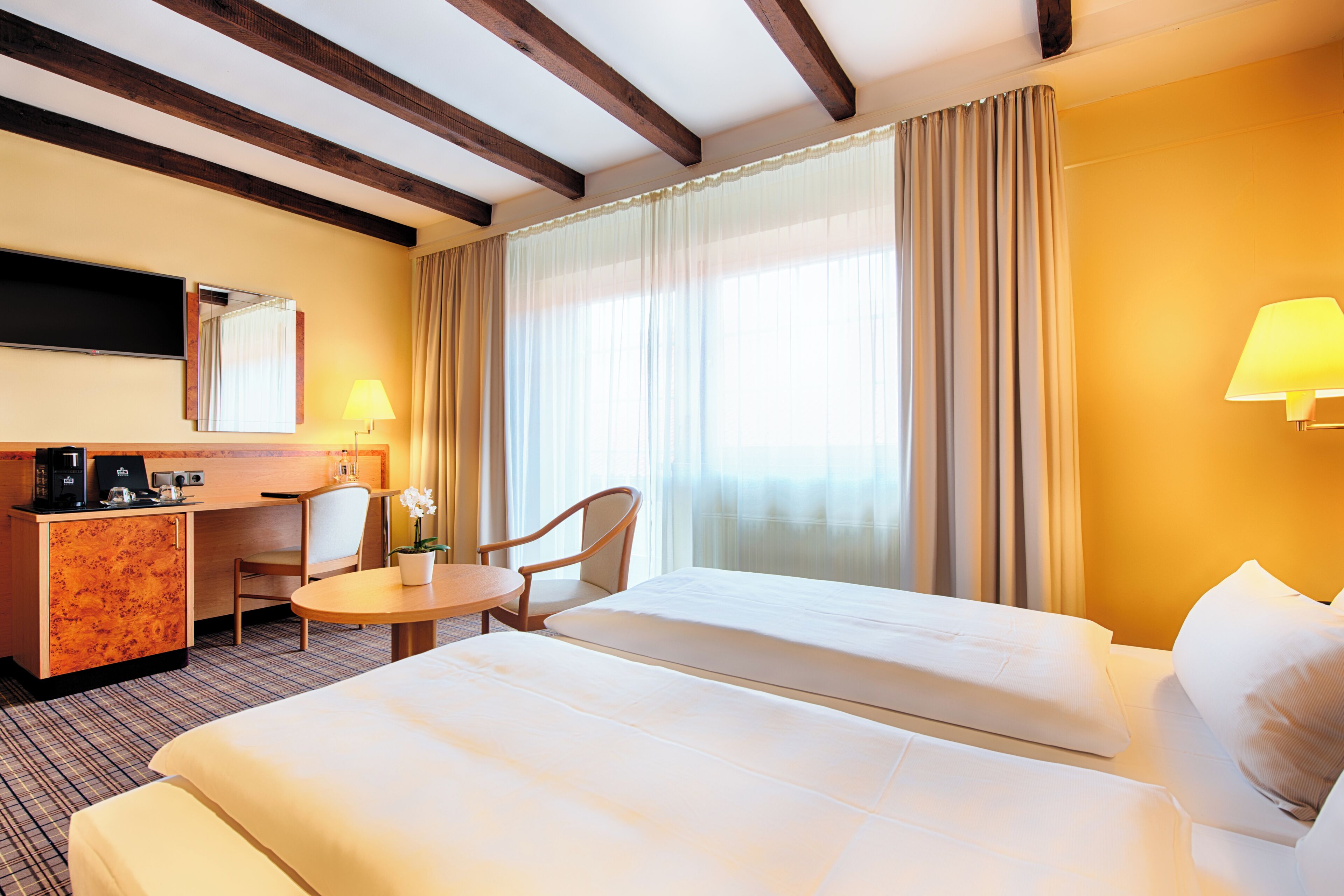Habitación de hotel con cama, escritorio con silla, una mesita, lámpara y televisor.