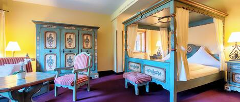 A four-poster bed with a canopy, a wooden bench, a small table, and a cabinet with decorative panels.