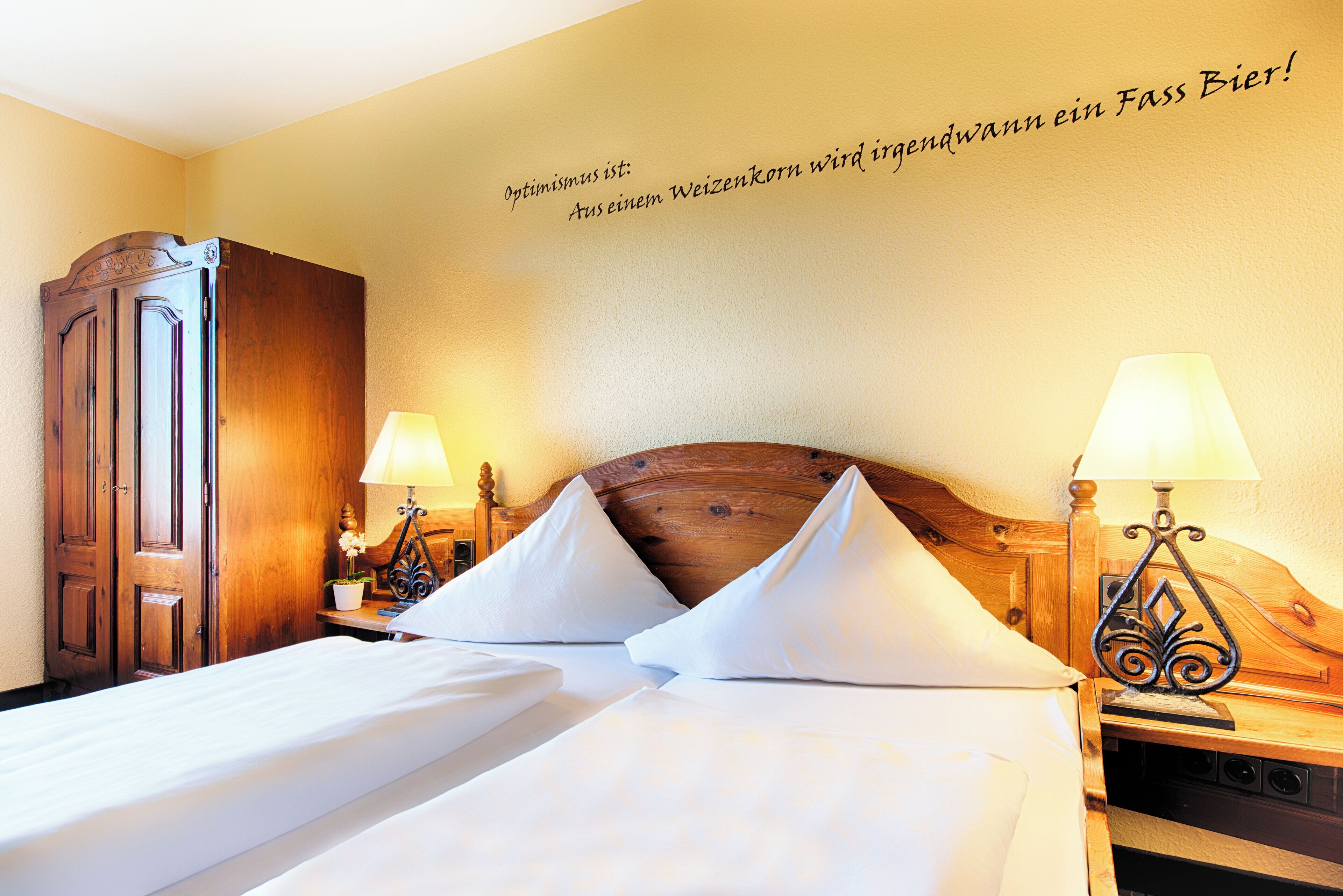 A hotel room with two beds, wooden headboards, bedside lamps, and a wall with a motivational quote.