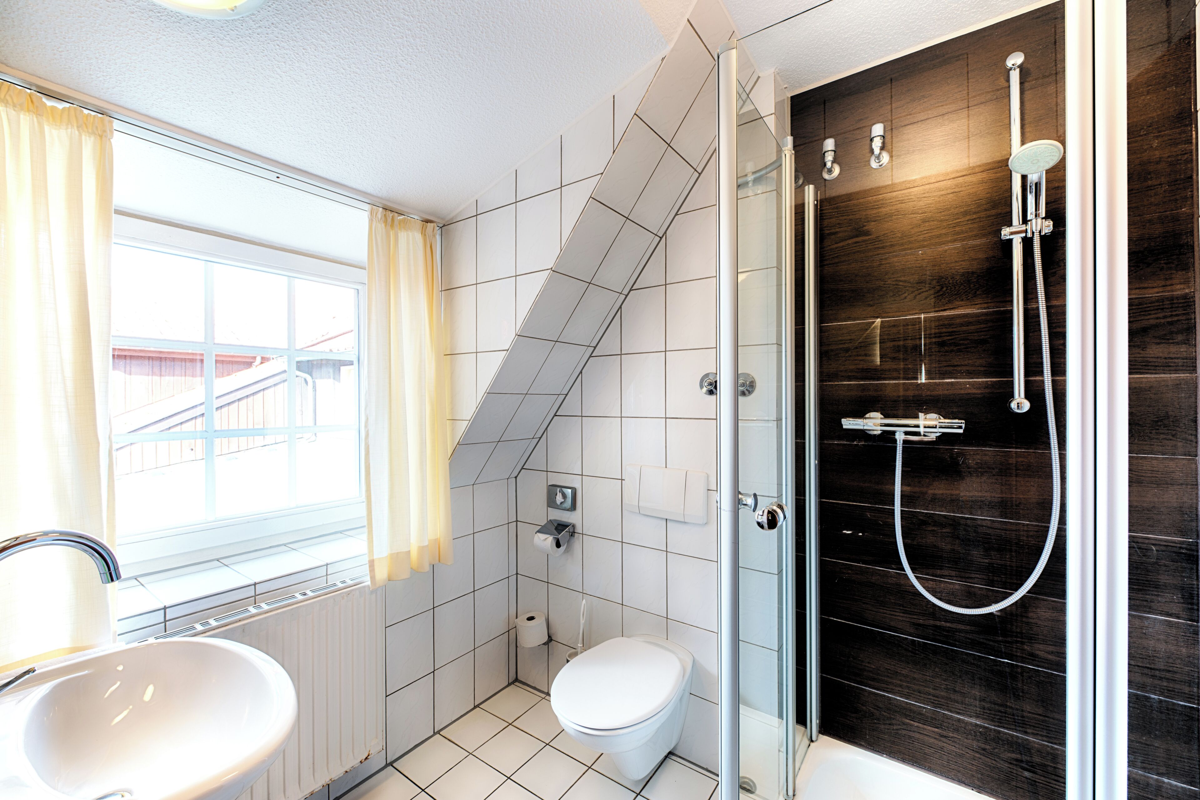 Un bagno con finestra, doccia, WC e lavandino.