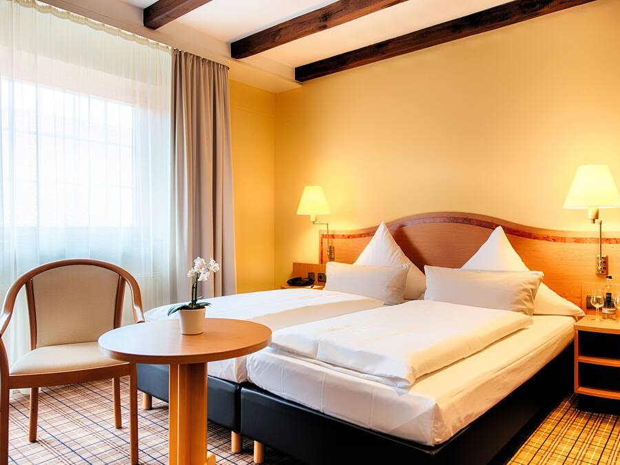 A hotel room with a double bed, a chair, a small table with a potted plant, and two bedside lamps.