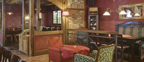 A cozy restaurant with wooden beams, brick walls, and a mix of wooden and upholstered chairs.