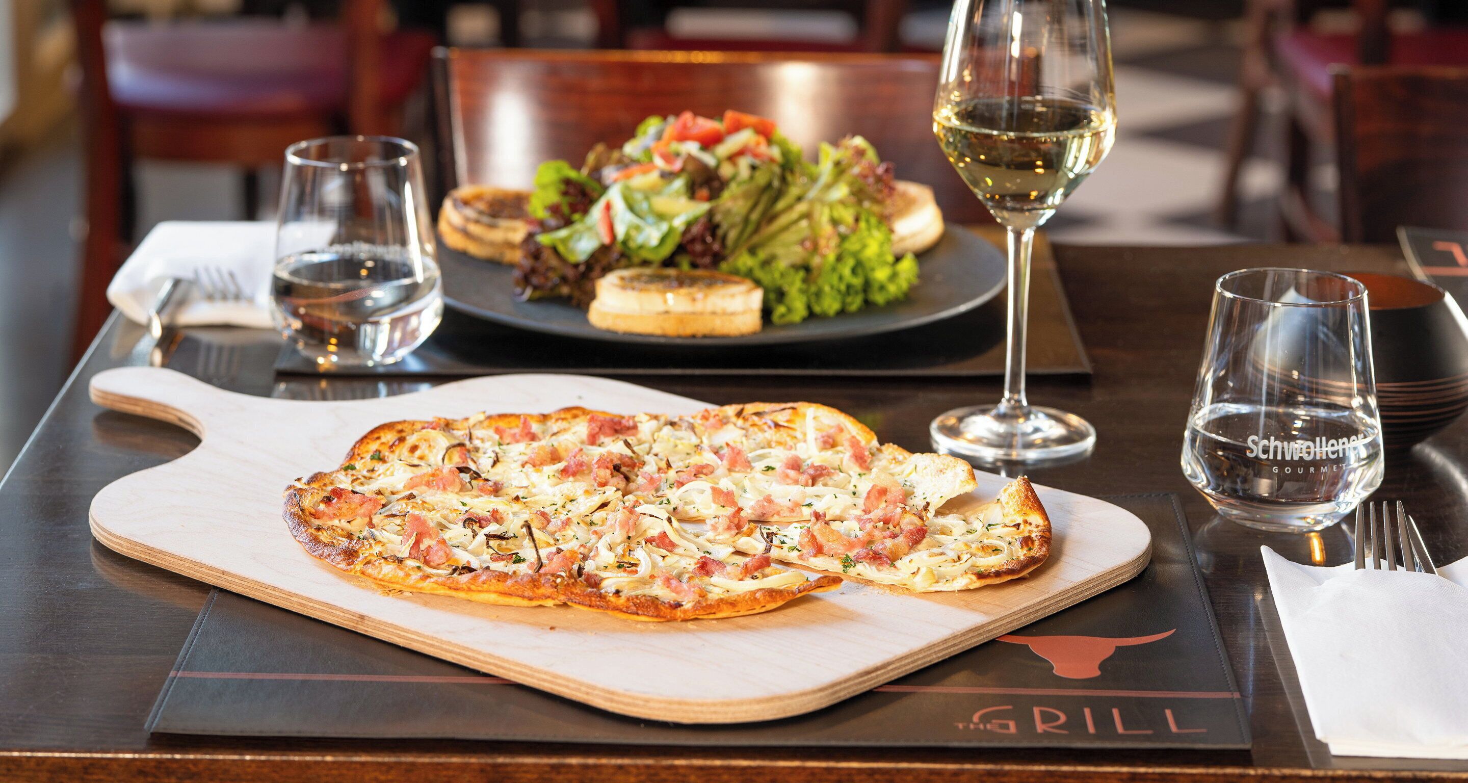 A dining table with a pizza, salad, and wine glasses.