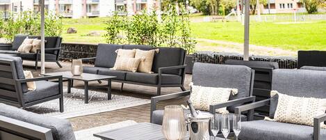 An outdoor seating area with grey sofas and tables, a champagne bucket, and glasses.