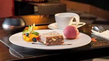 Un plato de postre con una porción de pastel, una bola de helado y fruta fresca sobre un plato blanco.