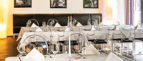 A restaurant setting with tables set for dining, clear glass chairs, and framed pictures on the wall.