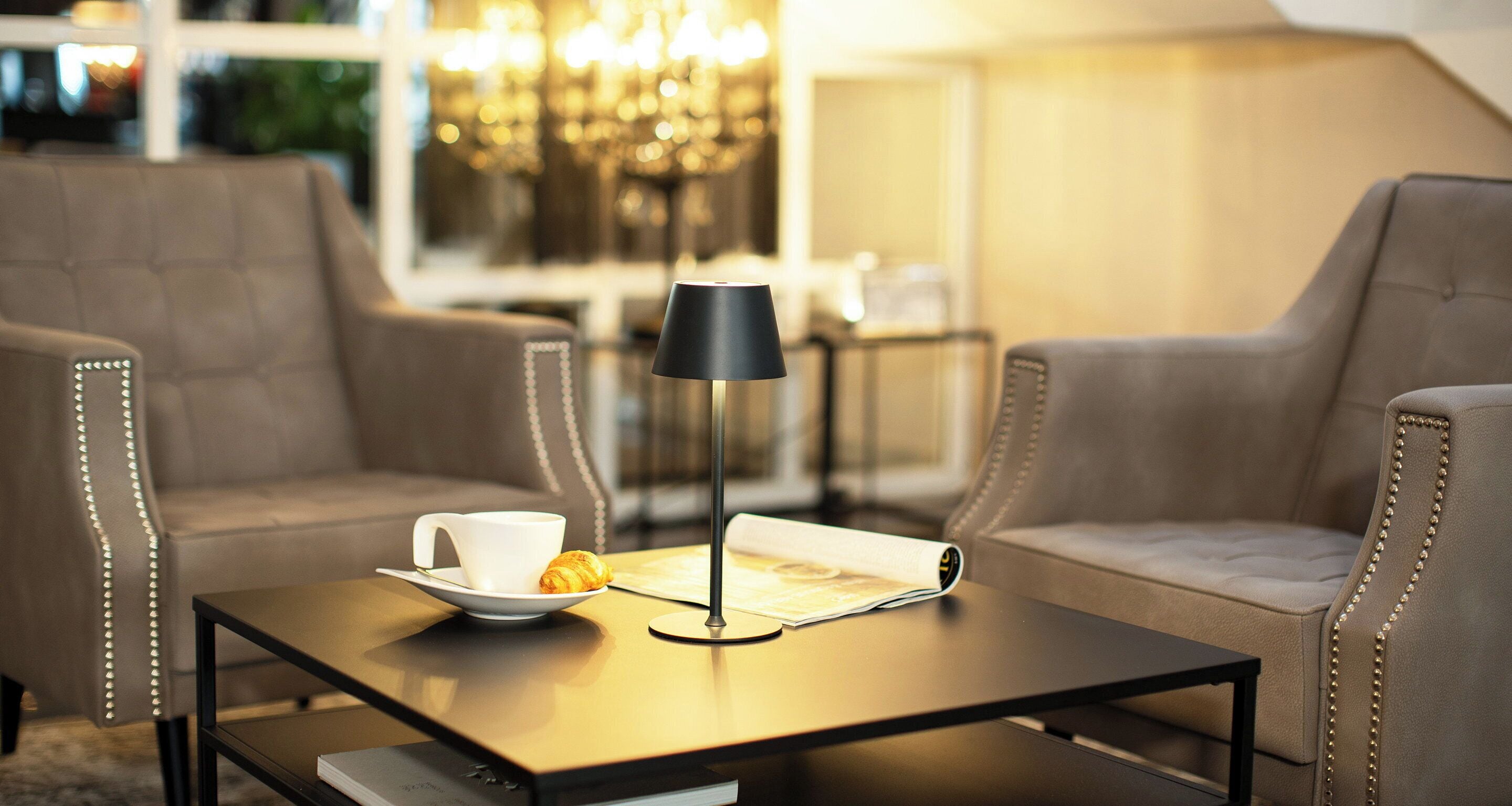 A cozy seating area with a table, a cup, a croissant, and a lamp.