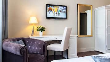 Een hotelkamer met een donkerbruine bank, een wit bureau, een aan de muur bevestigde televisie, een witte kledingkast en een spiegel.