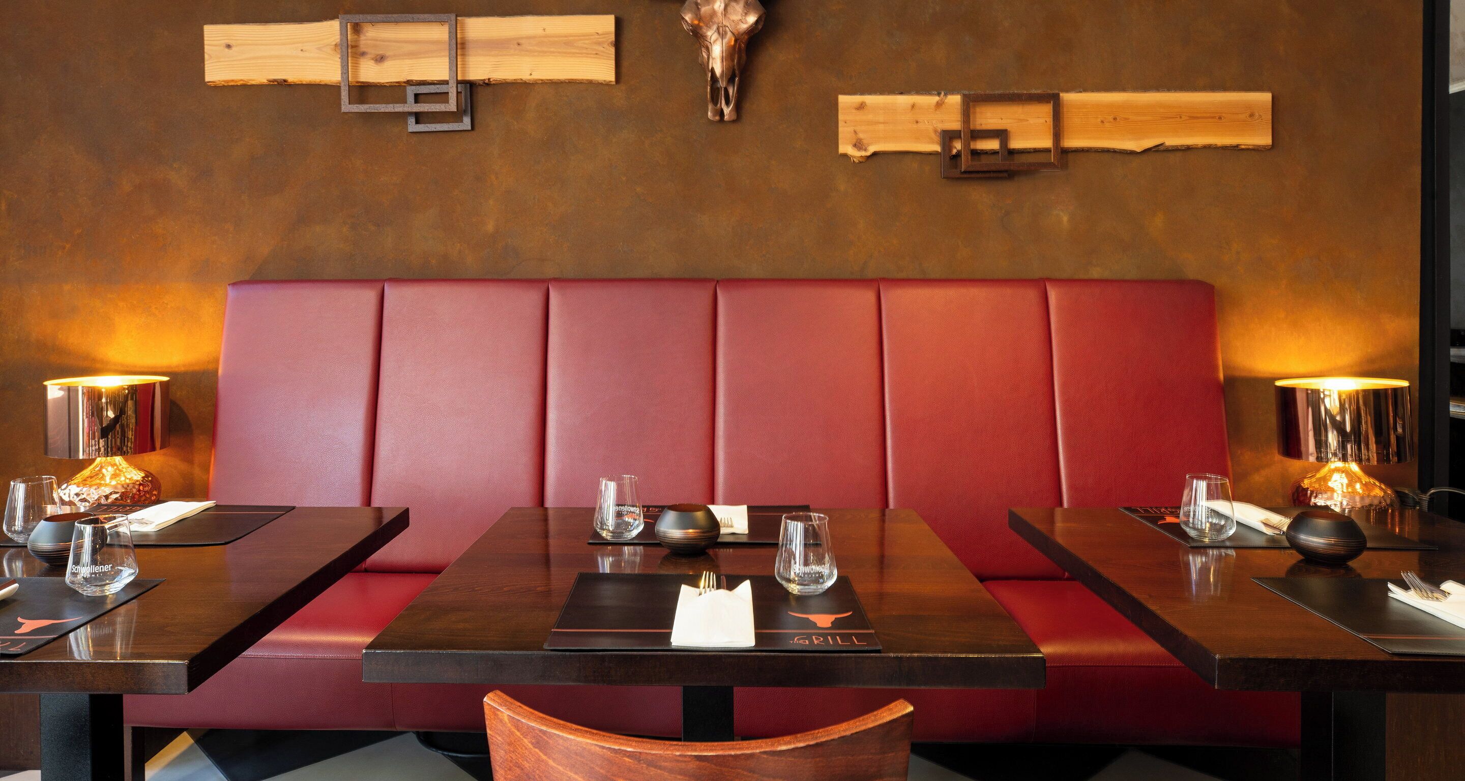 Un ristorante con sedute a cabina, tavoli di legno e una panca imbottita rossa.