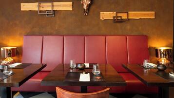 Un ristorante con sedute a cabina, tavoli di legno e una panca imbottita rossa.