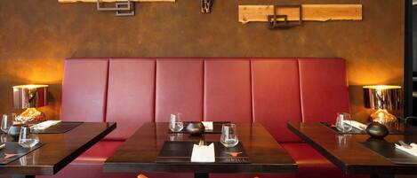 Un restaurante con cabinas, mesas de madera y un banco acolchado rojo.