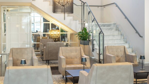 A spacious lobby with a staircase, leather armchairs, and a chandelier.