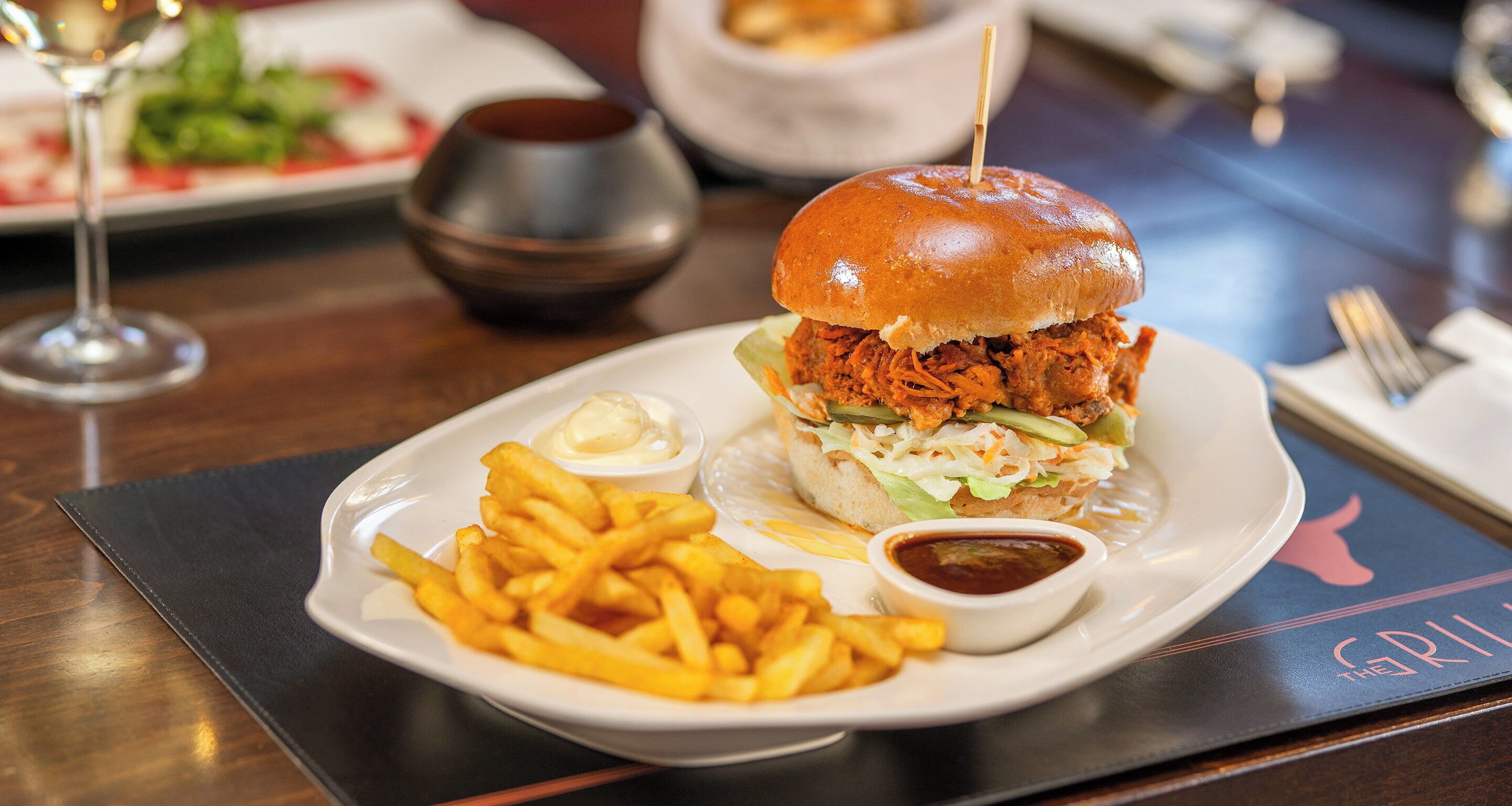 A plate with a pulled pork sandwich, fries, and two dipping sauces.