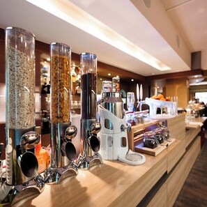 Una cafetería con varios dispensadores, incluyendo un molinillo y espumador, y una variedad de condimentos y utensilios sobre la barra.