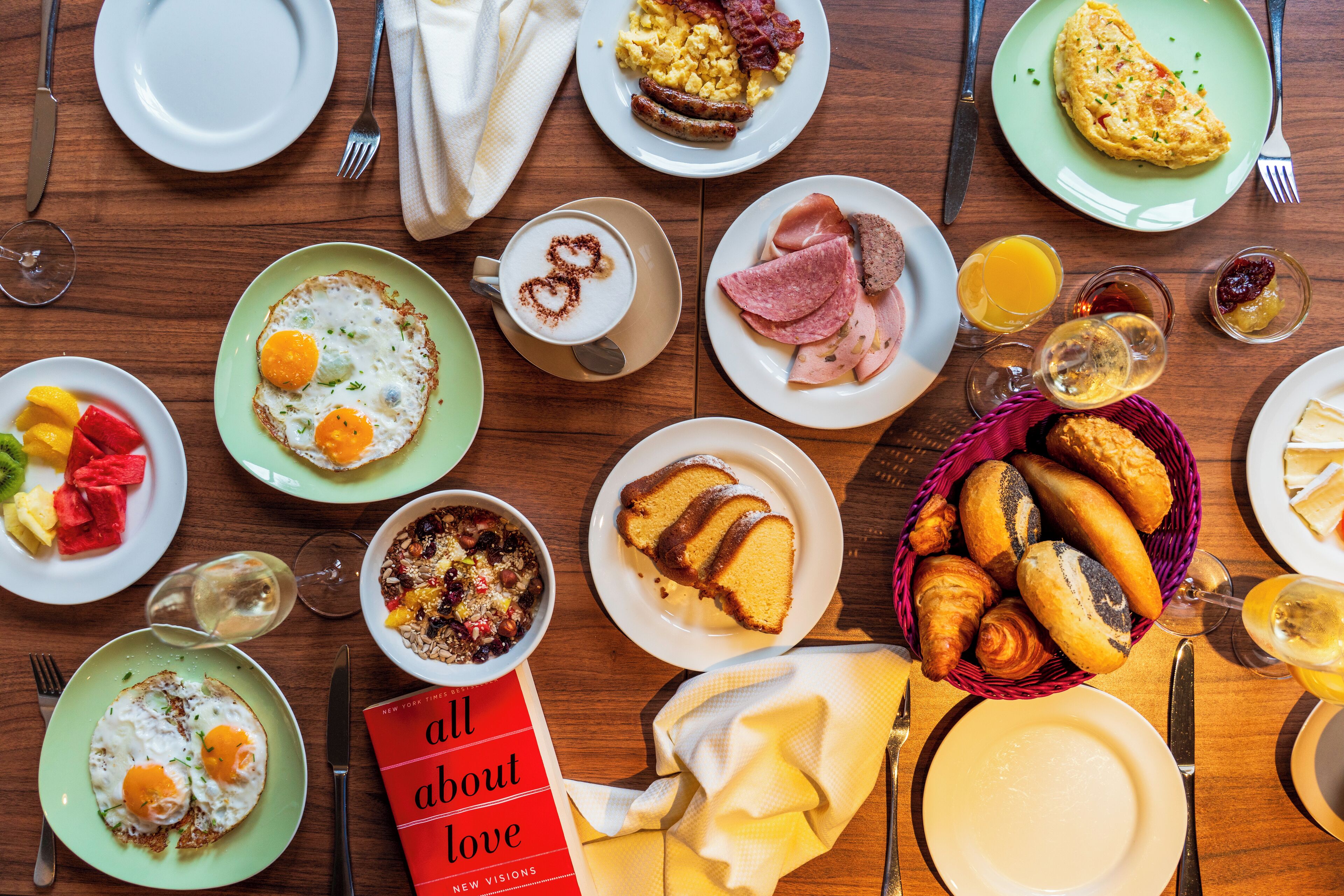 A breakfast setting with various dishes, including eggs, toast, and pastries, on a wooden table.
