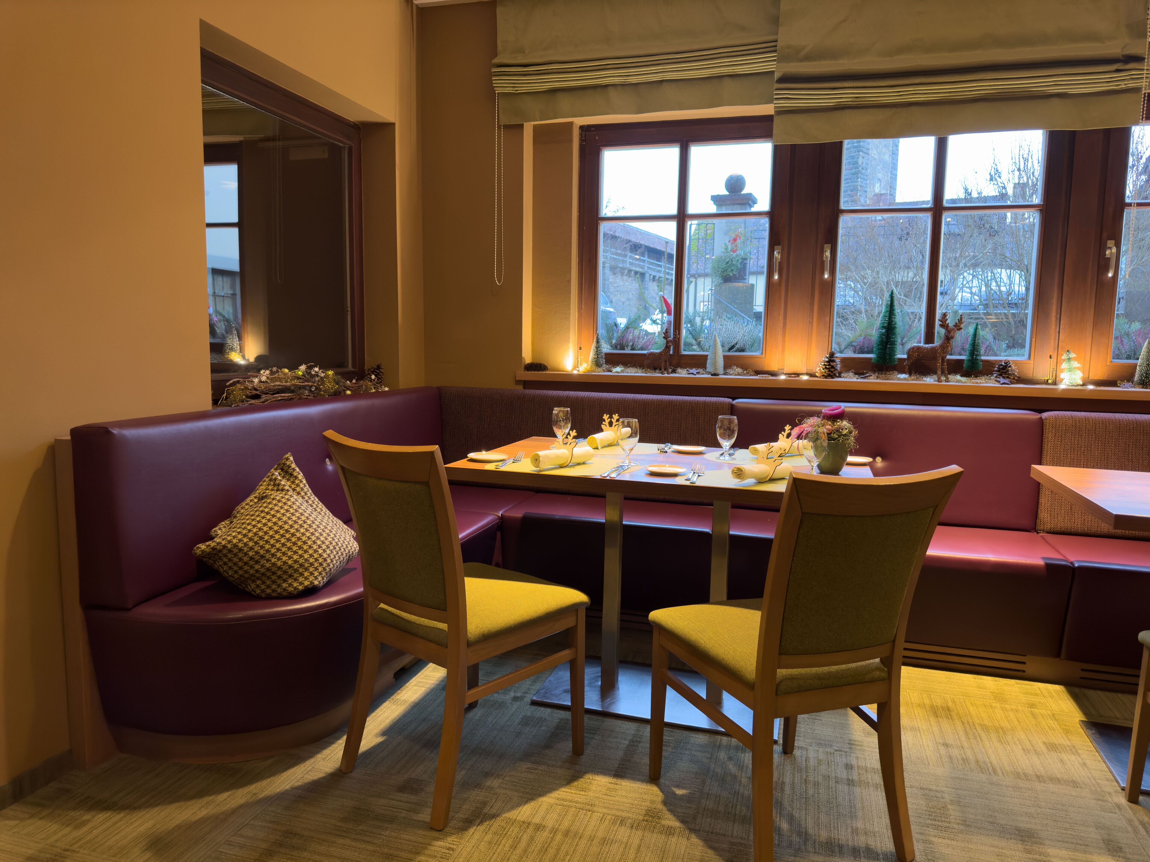 Un comedor acogedor con una mesa de madera dispuesta para dos personas, rodeado de asientos con cojines.