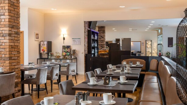 A modern cafe with tables and chairs, a brick wall, and a television mounted on the wall. - ibis Styles Rosenheim (Rosenheim)